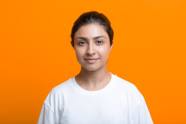 Retrato de mujer india adulta joven sonriente positiva en camiseta fondo naranja