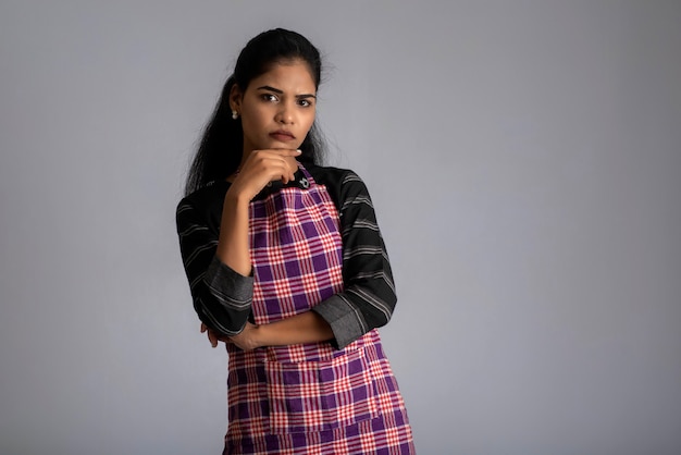 Retrato de mujer india chef o cocinera en un delantal, presentando, señalando, con signo ok, pulgar hacia arriba en el gris.