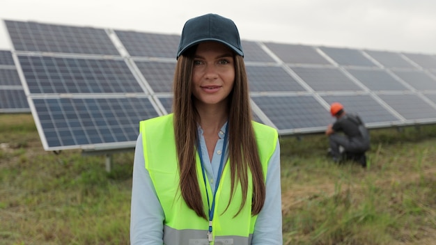 Retrato de mujer de ingeniero inspector en ropa de trabajo de pie junto al campo de paneles solares. Producción de energía limpia. Energía verde. Granja solar ecológica.