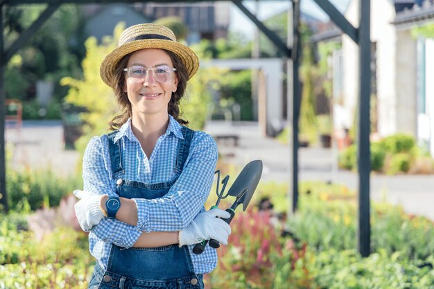 Retrato de mujer jardinera sonriente sosteniendo herramientas de jardín