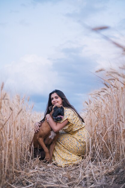 Retrato de una mujer joven abrazando a su perro en medio de un campo de trigo. Concepto de naturaleza y animales.