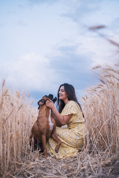 Retrato de una mujer joven abrazando a su perro en medio de un campo de trigo. Concepto de naturaleza y animales.