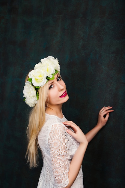 Retrato de mujer joven alegre atractiva en vestido blanco y corona de flores