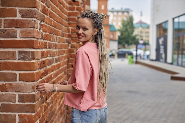 Retrato de una mujer joven alegre en una camiseta rosa en el contexto de una calle de la ciudad camina ...