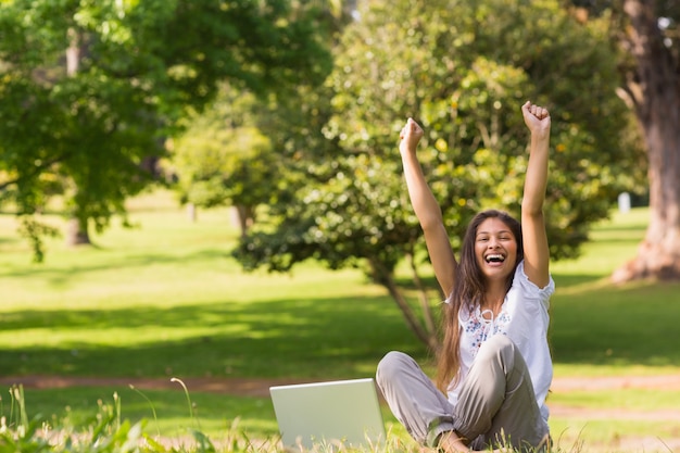 Foto retrato de una mujer joven alegre levantando las manos con la computadora portátil en el parque