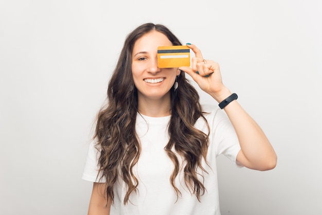 Retrato de mujer joven alegre sonriendo y cubriendo los ojos con tarjeta de crédito