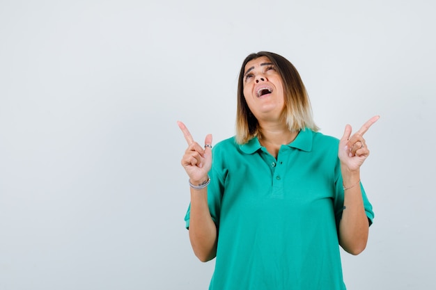 Retrato de mujer joven apuntando hacia arriba, mirando hacia arriba en una camiseta de polo y mirando desconcertado vista frontal