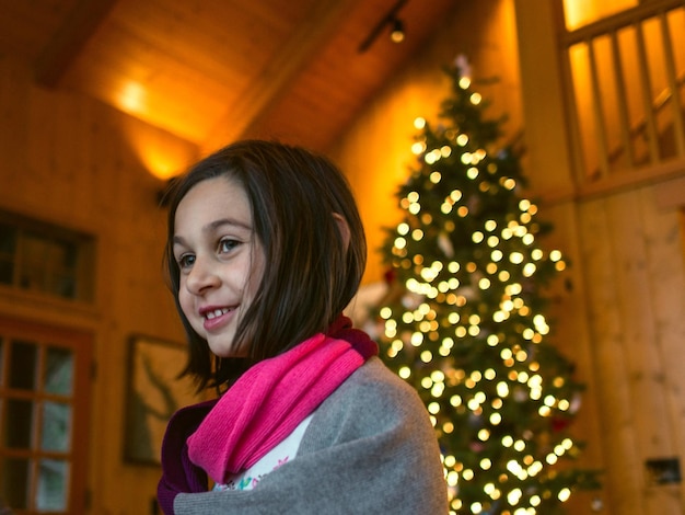 Retrato de una mujer joven en un árbol de Navidad iluminado