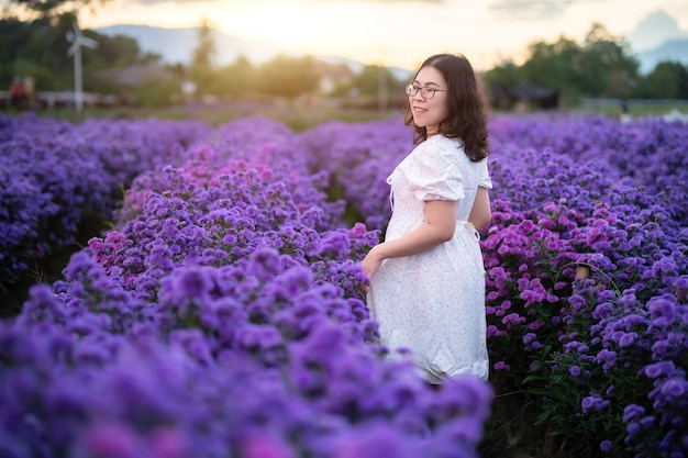 Retrato de mujer joven asiática feliz viajera con vestido blanco disfrutando en flor blanca o campo de flores púrpura Michaelmas Daisy en el jardín natural de Chiang MaiTailandiaviajar vacaciones relajantes