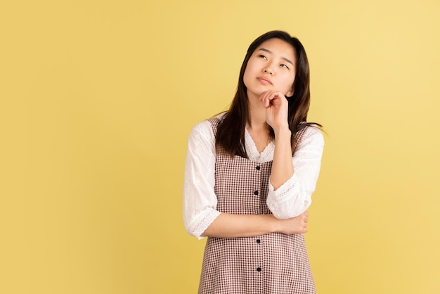 Retrato de mujer joven asiática sobre fondo de estudio amarillo Concepto de emociones humanas expresión facial anuncio de ventas para jóvenes