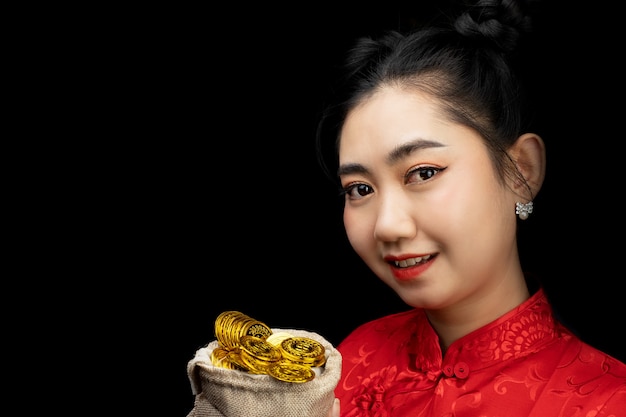 Retrato de mujer joven asiática vestido rojo cheongsam tradicional sosteniendo una moneda de oro en un saco