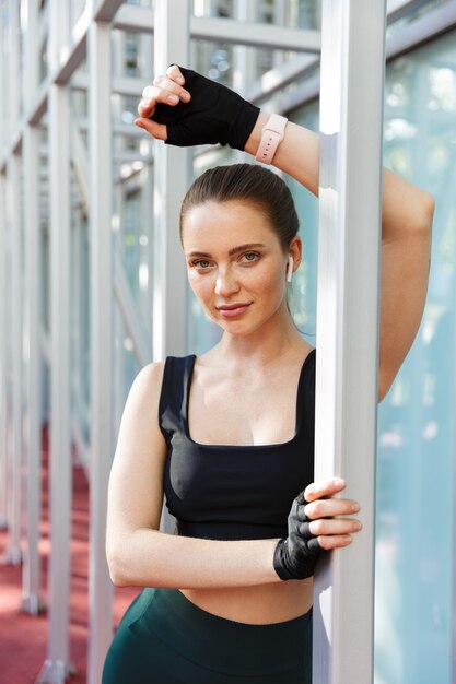 Retrato de mujer joven atlética vistiendo chándal haciendo ejercicio con barra de metal horizontal en el campo de deportes en el parque verde