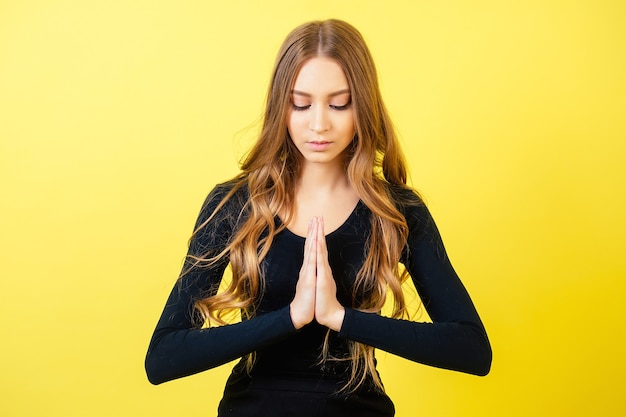 Foto retrato de una mujer joven y atractiva con cabello largo practicando yoga y meditando en el estudio sobre un fondo amarillo. concepto de tranquilidad y relajación