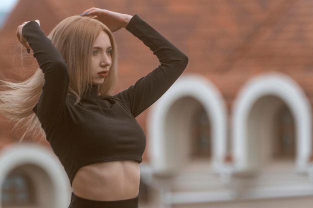 Retrato de una mujer joven y atractiva con cabello largo y rubio que usa una blusa negra y se ajusta el cabello