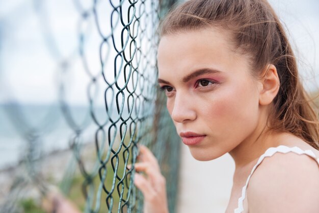 Foto retrato de mujer joven atractiva mirando a través de la valla de alambre