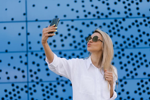 Retrato de una mujer joven y atractiva que se toma una selfie con un smartphone de fondo azul