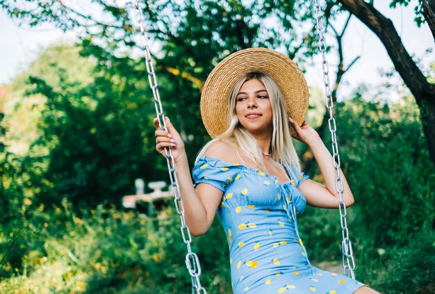 Retrato de mujer joven atractiva con sombrero de paja al aire libre en un día soleado de verano en un columpio.