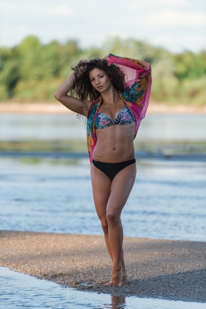 Foto retrato de una mujer joven en bikini de pie en la playa