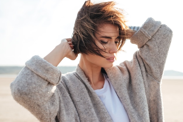 Retrato de mujer joven y bonita en abrigo posando junto al mar en otoño