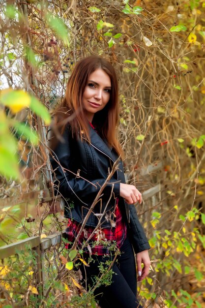 Retrato de mujer joven y bonita de apariencia eslava en ropa casual oscura en otoño, de pie en el increíble parque en la valla. Modelo lindo paseos en el parque en otoño dorado con el telón de fondo de la naturaleza y la carretera