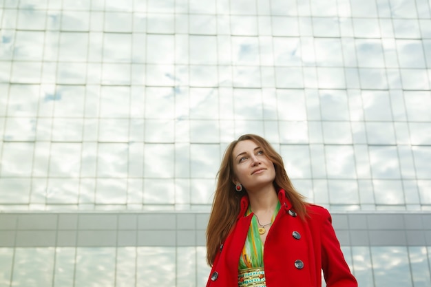 Retrato de mujer joven y bonita de apariencia eslava con vestido amarillo y abrigo rojo. Fachada del edificio comercial