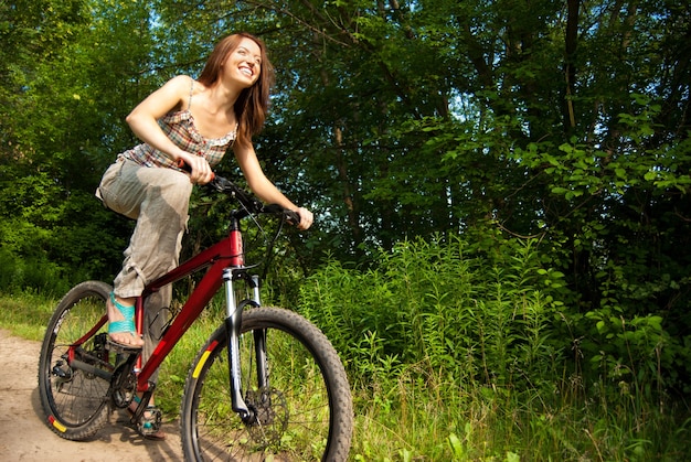 Retrato de mujer joven y bonita con bicicleta en un parque sonriendo - Al aire libre