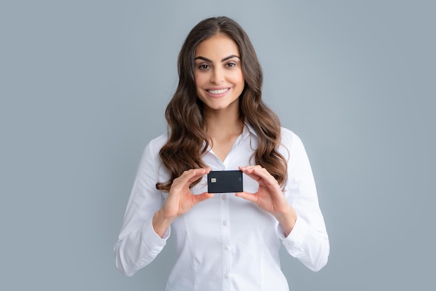 Retrato de una mujer joven y bonita en camisa con tarjeta de crédito sobre fondo gris Chica alegre demostrando solución de tarjeta bancaria