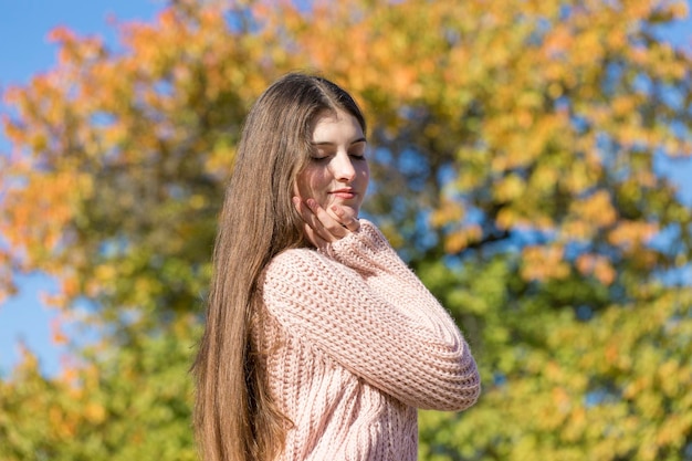 Retrato de una mujer joven y bonita con un elegante suéter tejido de pie en el bosque dorado de otoño en un día soleado