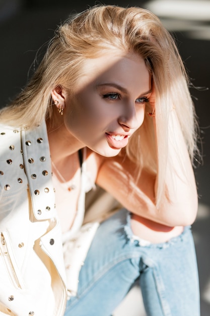 Retrato de una mujer joven y bonita feliz con hermosos ojos azules con cabello rubio con labios regordetes sexy en una chaqueta de cuero de primavera de moda en un día soleado