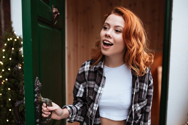 Retrato de una mujer joven y bonita con el pelo rojo abre la puerta. Mirando a un lado.