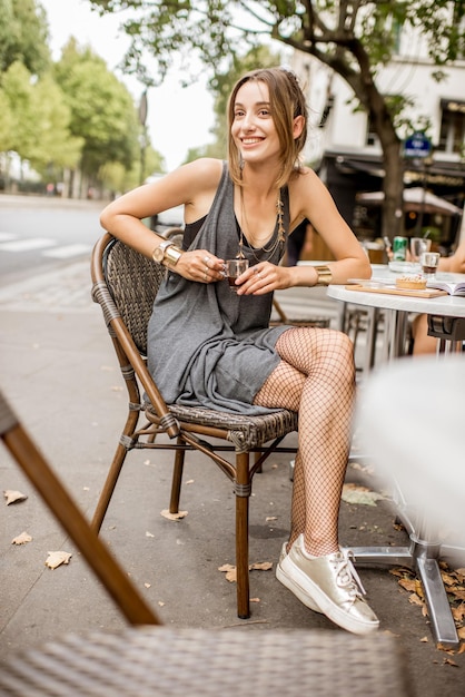 Retrato de una mujer joven y bonita en vestido gris y medias de cabaret sentado al aire libre en el café francés