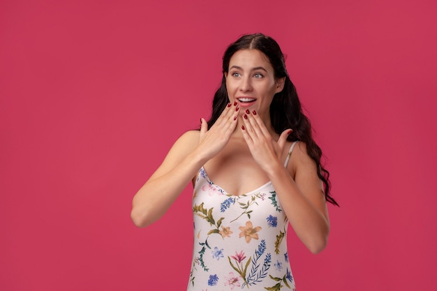 Retrato de una mujer joven y bonita con un vestido ligero de pie sobre fondo rosa en estudio. Personas sinceras emociones.