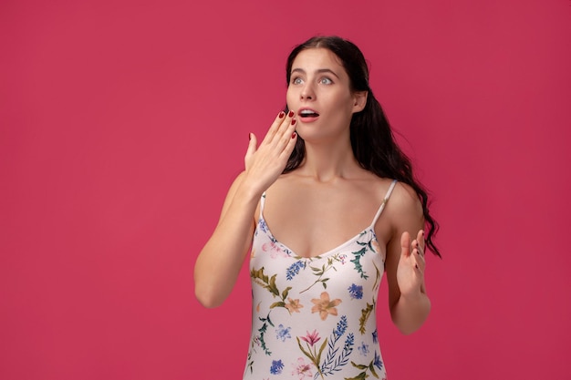 Retrato de una mujer joven y bonita con un vestido ligero de pie sobre fondo rosa en estudio. Personas sinceras emociones.