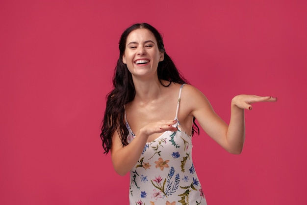 Retrato de una mujer joven y bonita con un vestido ligero de pie sobre fondo rosa en estudio. Personas sinceras emociones.