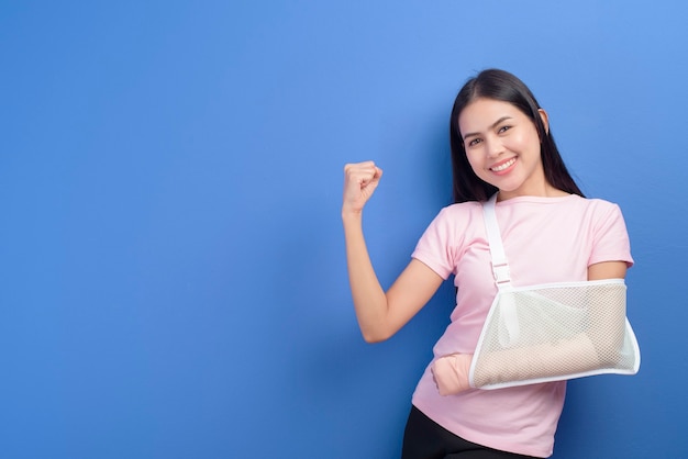 Un retrato de una mujer joven con un brazo lesionado en un cabestrillo sobre la pared azul