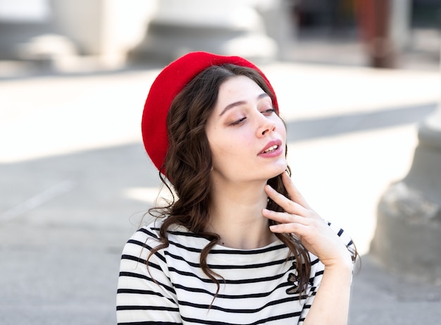 Retrato de una mujer joven con cabello largo y oscuro con una boina roja en el fondo de la ciudad.