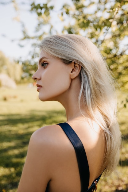 Retrato de una mujer joven con cabello rubio y ojos azules al aire libre en un parque