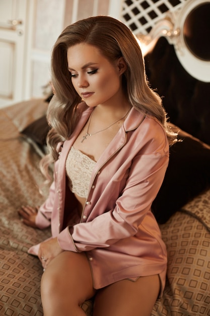 Retrato de mujer joven con cabello rubio platino en pijama de satén rosa en la cama.