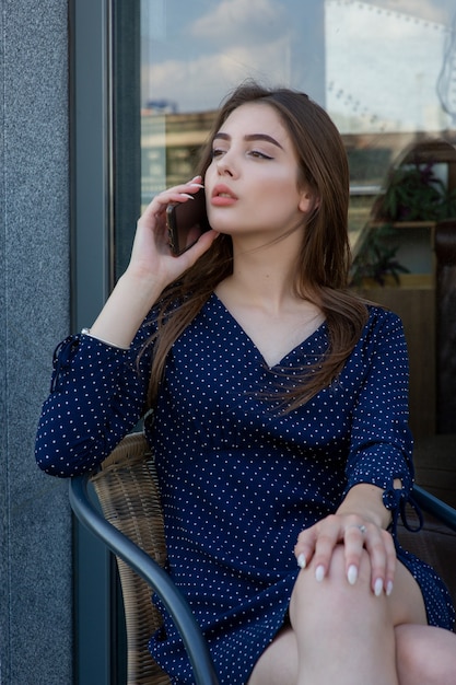 Retrato de una mujer joven en un café en la calle sentada en una mesa y hablando por teléfono.