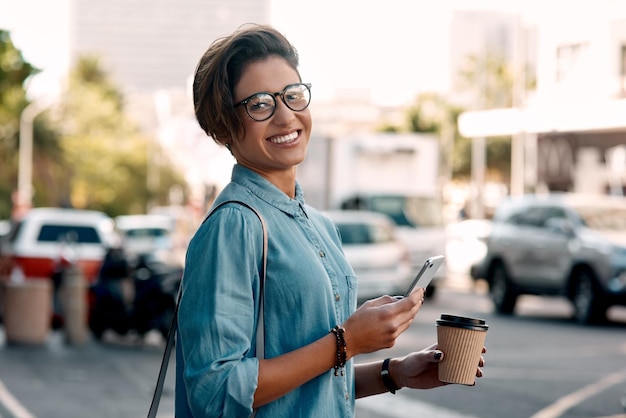 Retrato de mujer joven con café por la mañana en la ciudad y teléfono inteligente en el fondo de la calle Viaje con teléfono celular feliz y mujer con bebida en el área urbana o paisaje urbano