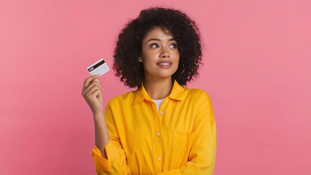 Foto retrato de una mujer joven con camisa amarilla mostrando una tarjeta de crédito y mirando hacia otro lado en el espacio de copia aislado