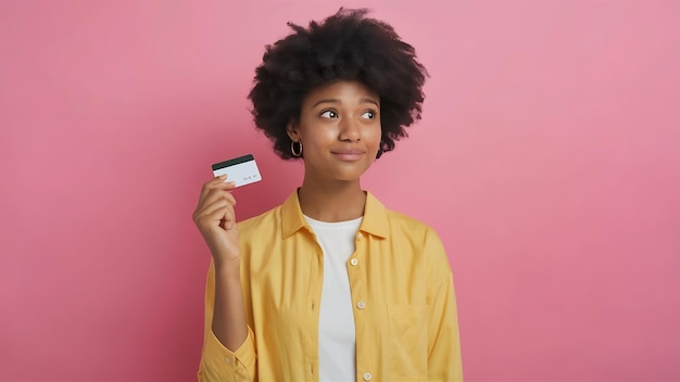 Retrato de una mujer joven con camisa amarilla mostrando una tarjeta de crédito y mirando hacia otro lado en el espacio de copia aislado