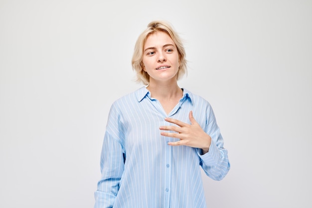 Retrato de una mujer joven con camisa azul sonriendo y haciendo un gesto sincero sobre un fondo blanco