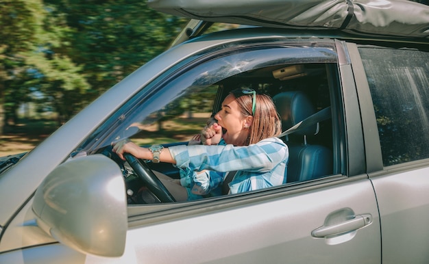 Retrato de mujer joven cansada conduciendo coche y bostezando después de un viaje demasiado largo. Riesgo y peligro en el concepto de carretera.