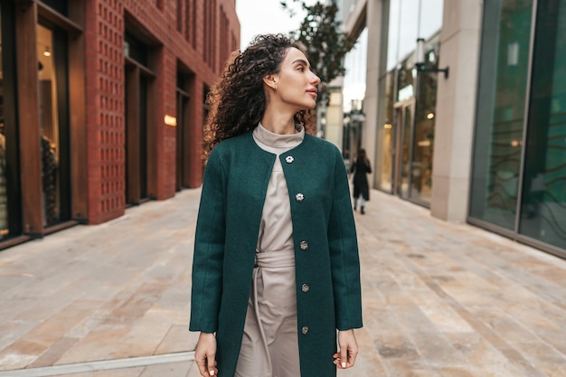 retrato, de, mujer joven, en, capa verde, con, pelo rizado, en la ciudad