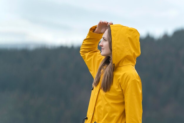 Retrato de mujer joven en chaqueta amarilla en la naturaleza mira a lo lejos Bosque en el fondo Vista lateral