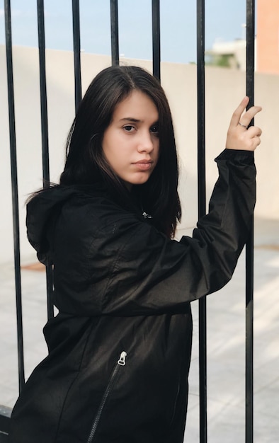 Foto retrato de una mujer joven con una chaqueta negra de pie junto a la barandilla