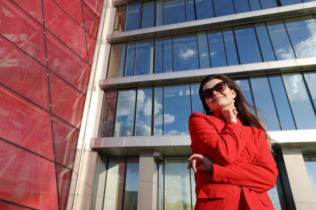 Retrato de una mujer joven con una chaqueta roja en el fondo de edificios de cristal