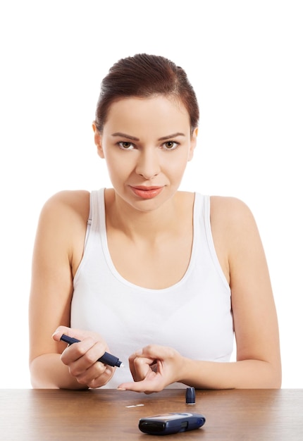 Foto retrato de una mujer joven chequeando la diabetes contra un fondo blanco