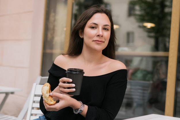 Retrato de una mujer joven comiendo un croissant y bebiendo café Desayuno de café de verano afuera